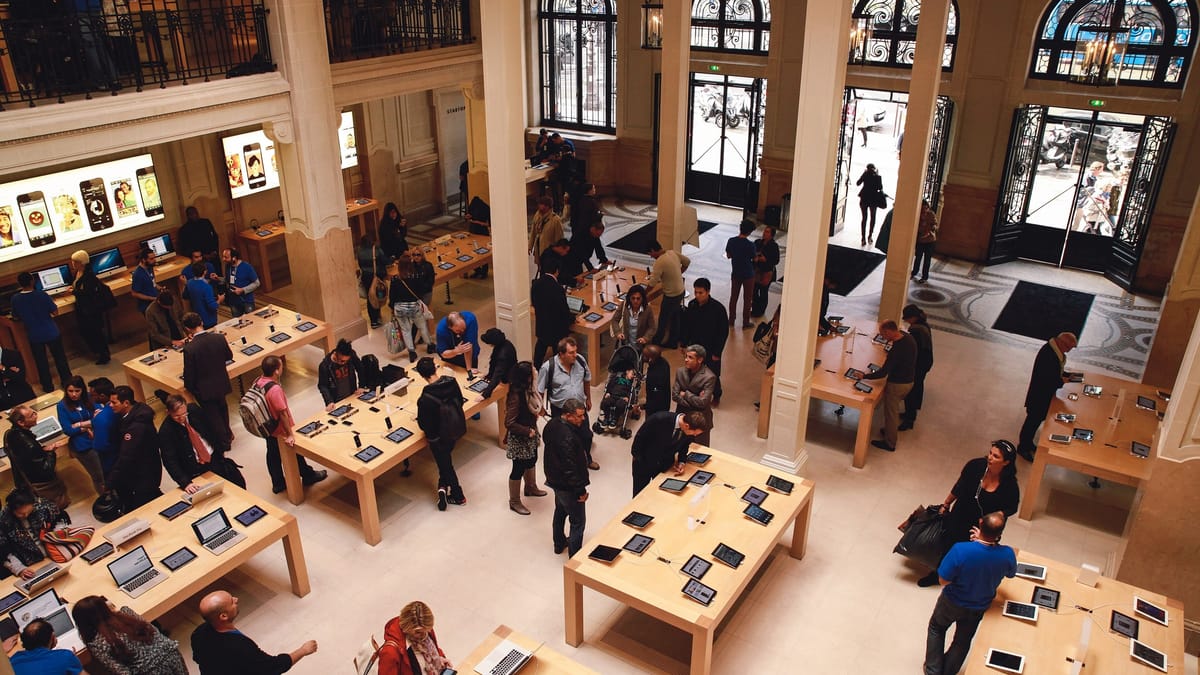 Intérieur de l'Apple Store Opéra à Paris vu d'en haut : tables d'appareils Apple en libre essai et visiteurs