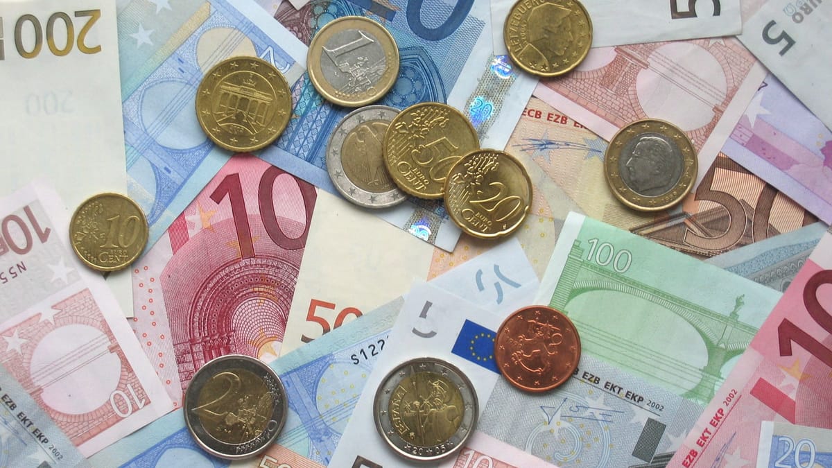 Billets en euros de plusieurs valeurs éparpillés, avec des pièces en euros posées dessus