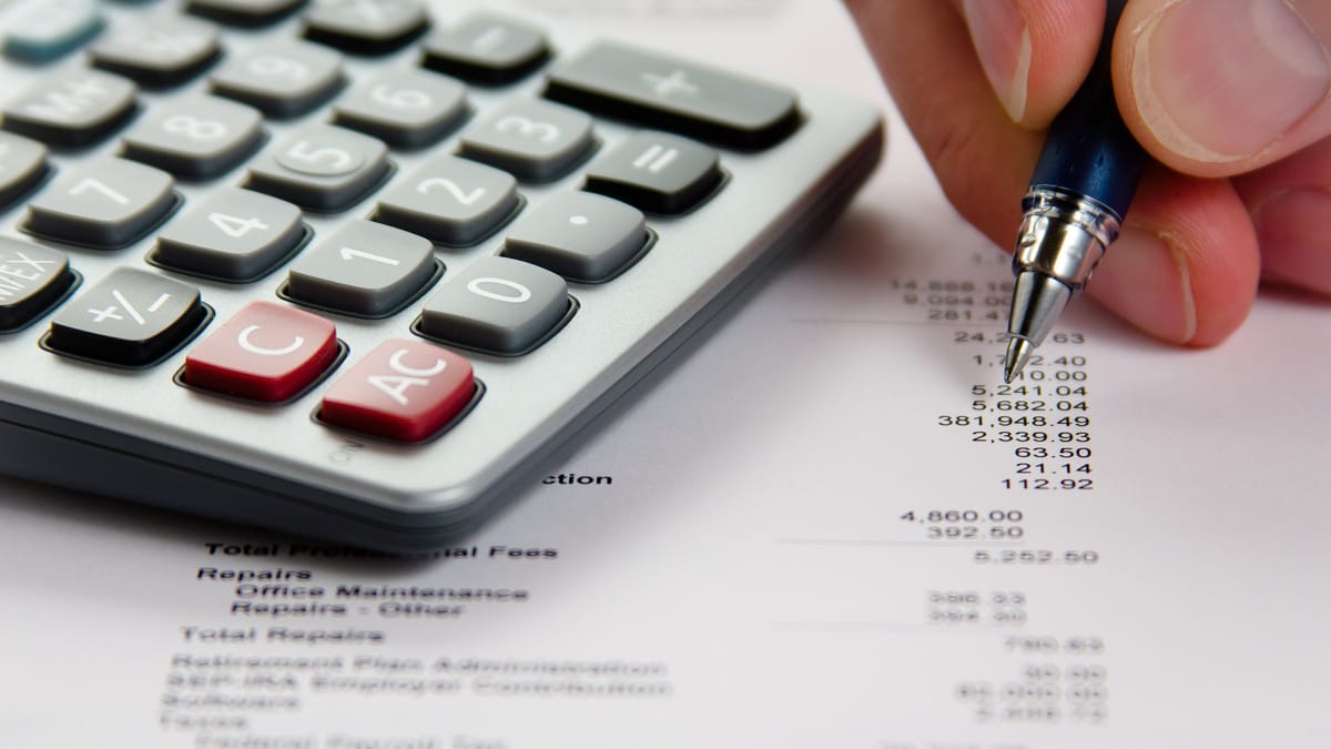 Gros plan sur une calculatrice et une main qui pointe avec un stylo une colonne de chiffres d'un état financier