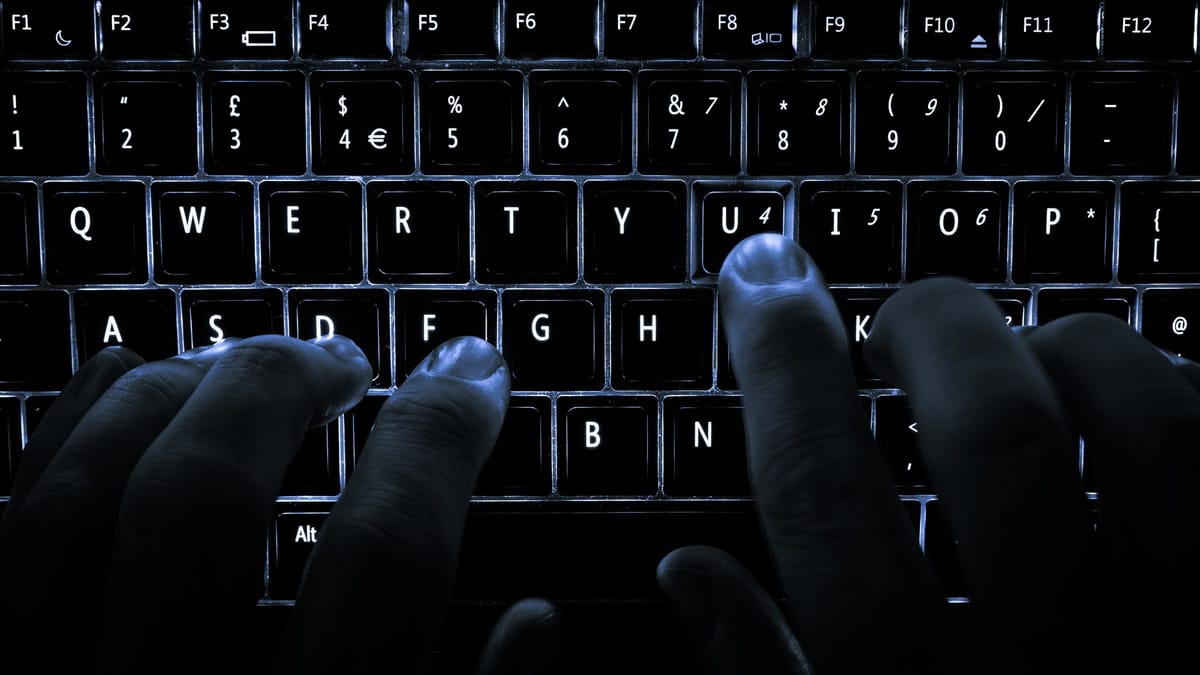 Mains posées sur le clavier rétroéclairé d'un ordinateur portable, dans la pénombre
