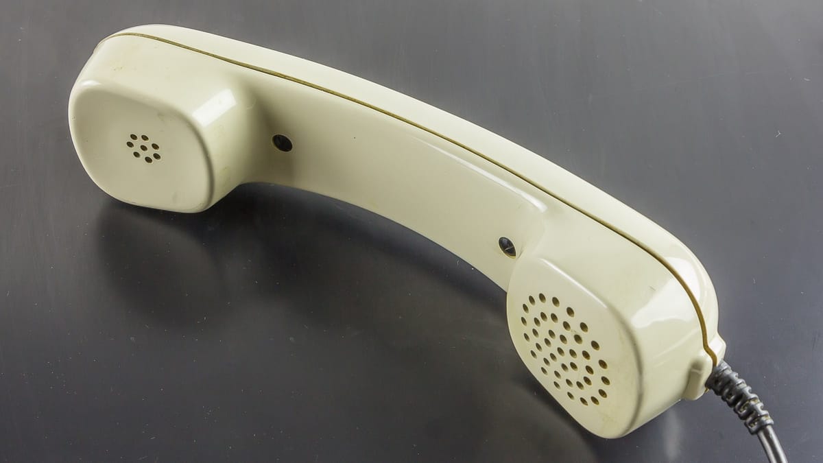Combiné de téléphone fixe beige, posé sur une surface sombre, vu de trois quarts avec son cordon torsadé