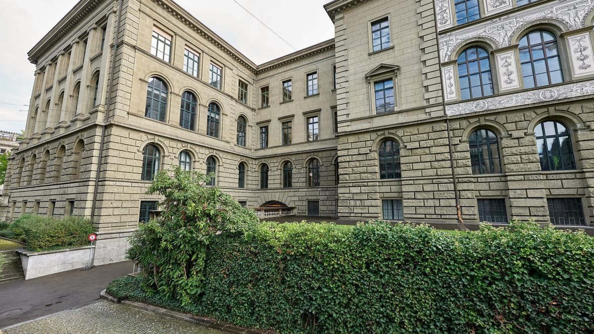 Façade en pierre du bâtiment principal de l'ETH Zurich, aux grandes fenêtres cintrées, bordée d'une haie