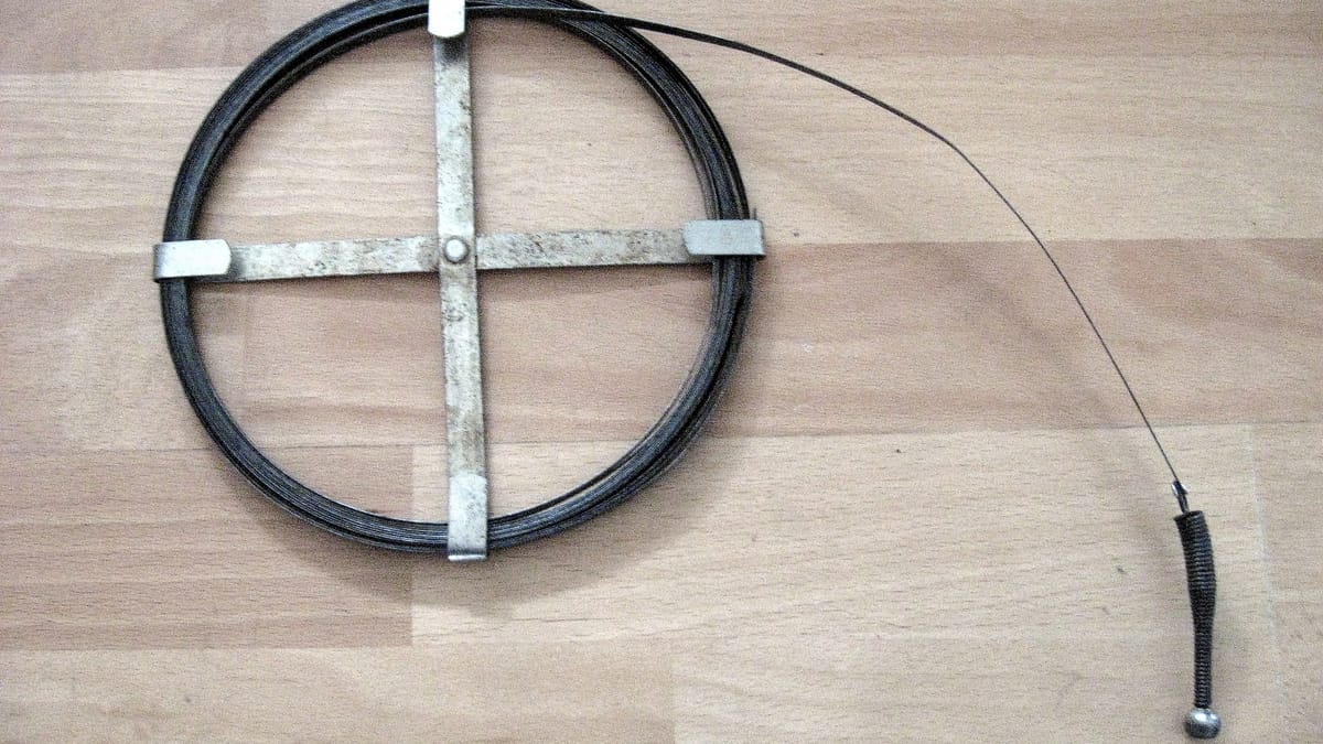 Furet de plombier enroulé sur son support métallique, posé sur une surface en bois clair