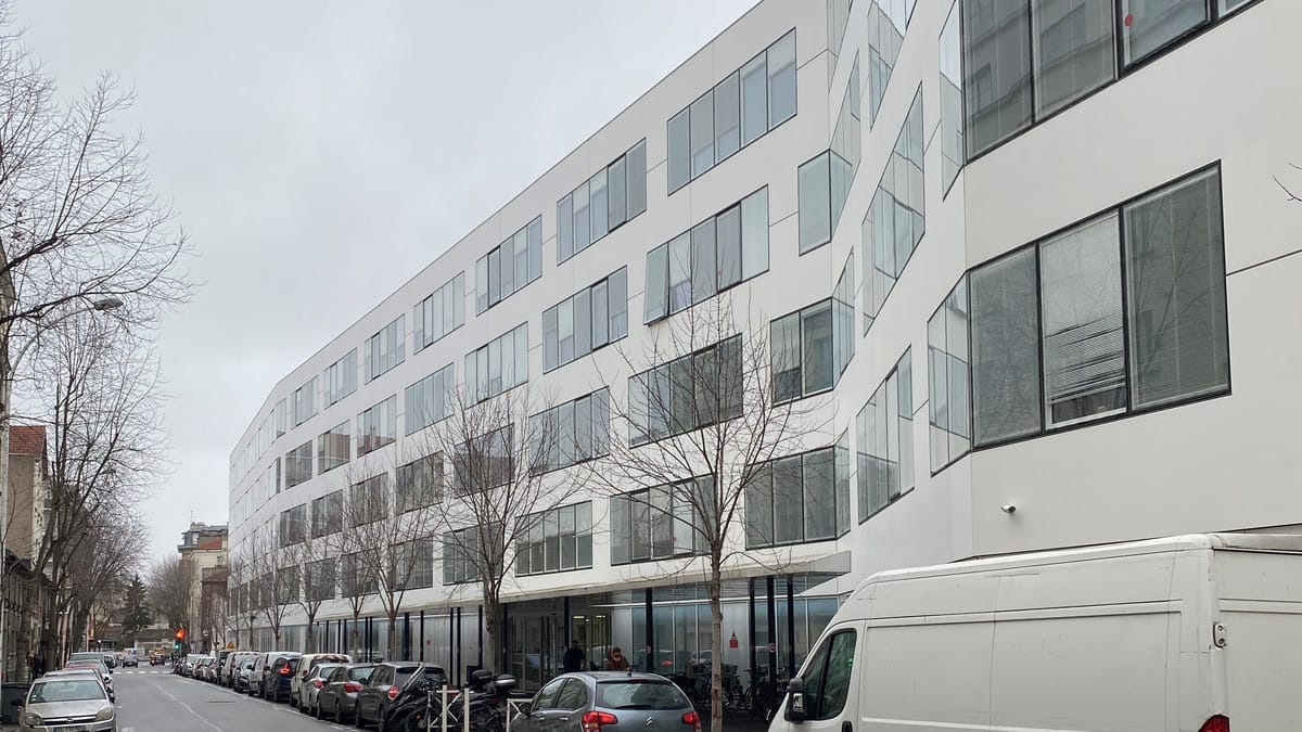 Façade blanche d’un immeuble de bureaux moderne aux grandes fenêtres, le long d’une rue bordée d’arbres et de voitures garées
