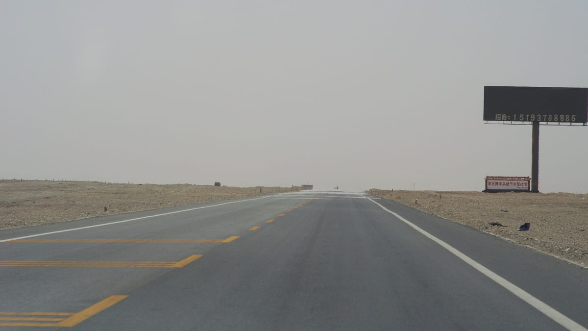 Route droite dans un désert dont l'asphalte, au loin, semble recouvert d'eau sous l'effet d'un mirage
