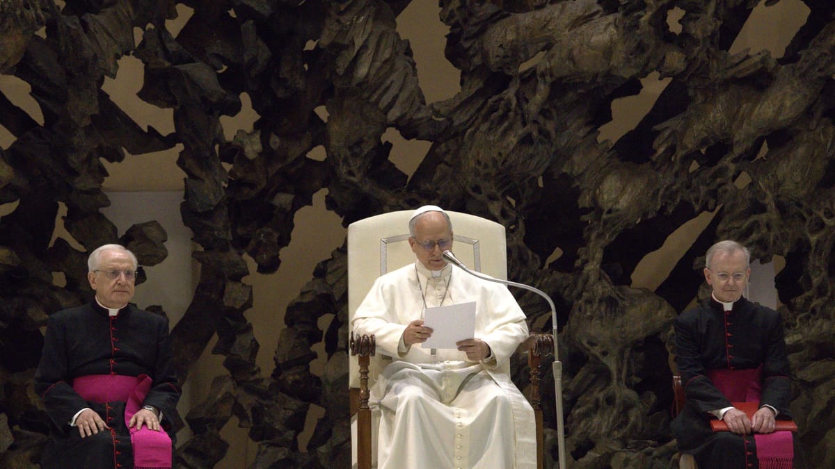 Le pape Léon XIV, en soutane blanche, lit un texte assis devant un micro, entouré de deux prélats, lors d’une audience au Vatican