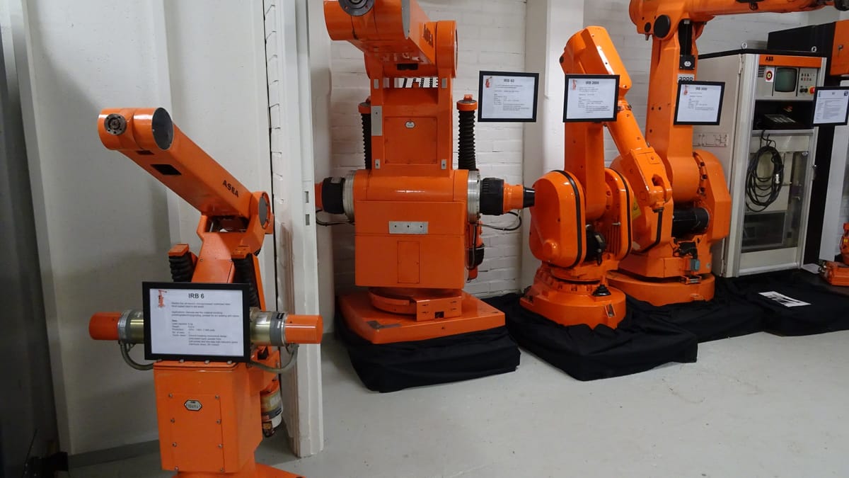 Plusieurs bras robotisés industriels orange de marque ASEA et ABB exposés côte à côte dans un musée, avec leurs panneaux explicatifs