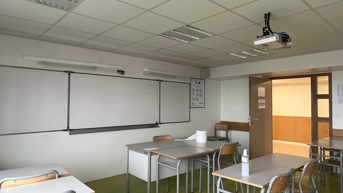 Salle de classe vide avec des tables, des chaises, un tableau blanc et un vidéoprojecteur fixé au plafond